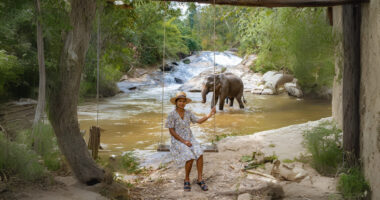Woman on swing by river with elephant at Chiang Mai sanctuary.